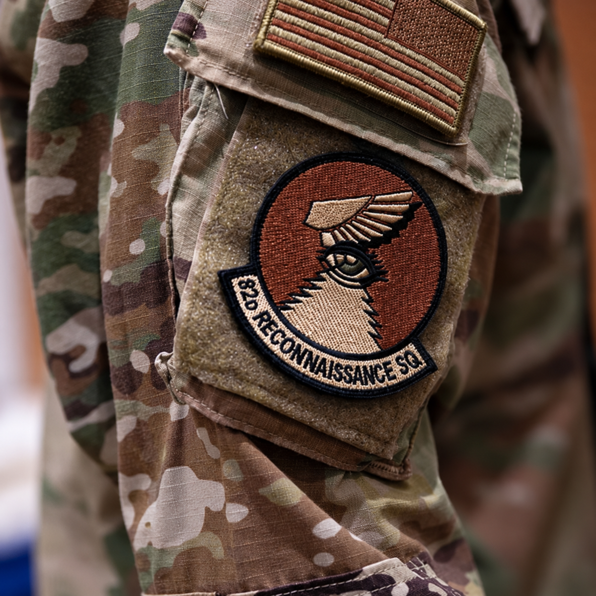 Winged-eye patch reading “82D RECONNAISSANCE SQ” on a camouflage sleeve beneath a U.S. flag patch.