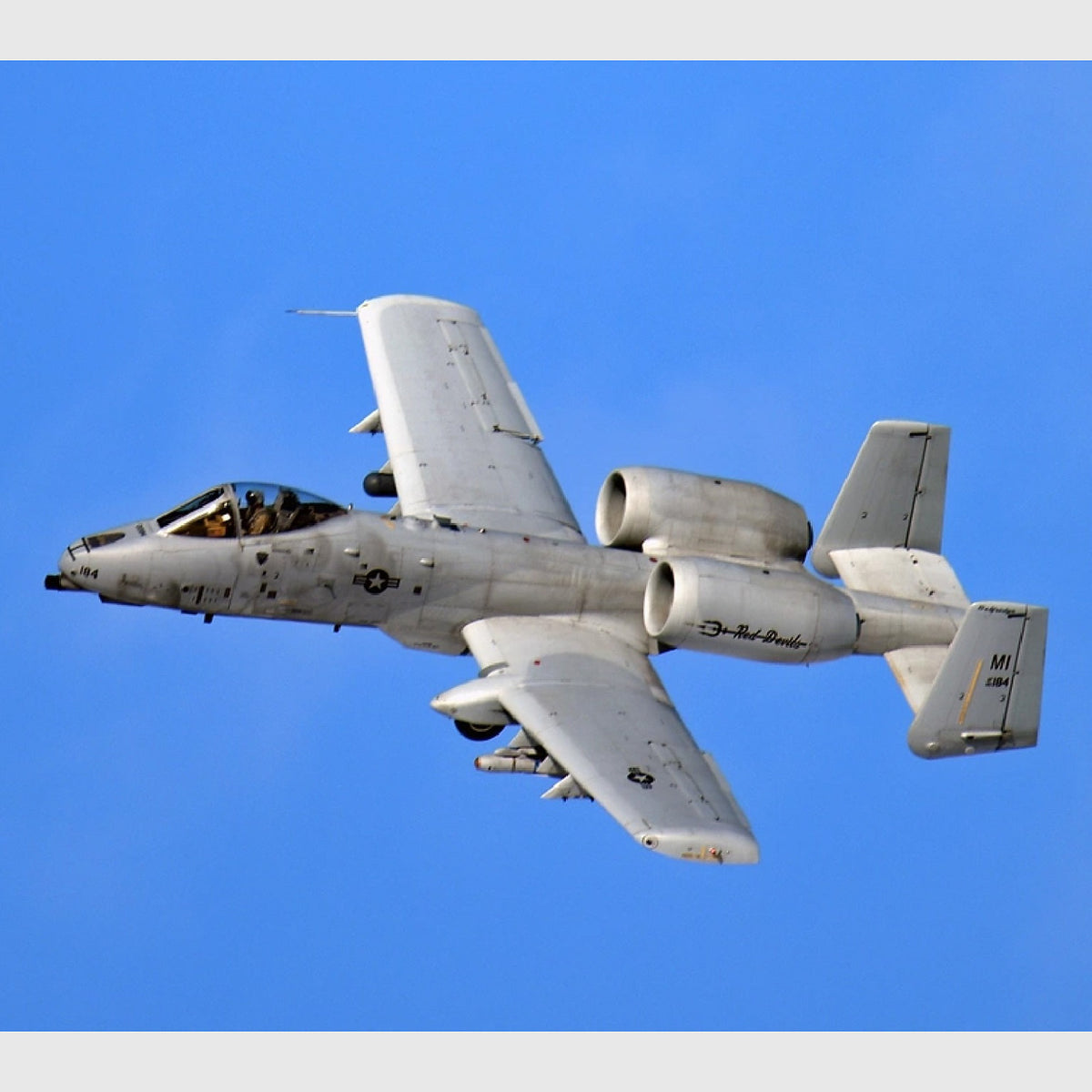A-10 Thunderbolt II banking against a clear blue sky, showing its straight wings, twin engines mounted above the fuselage, and twin tail fins.
