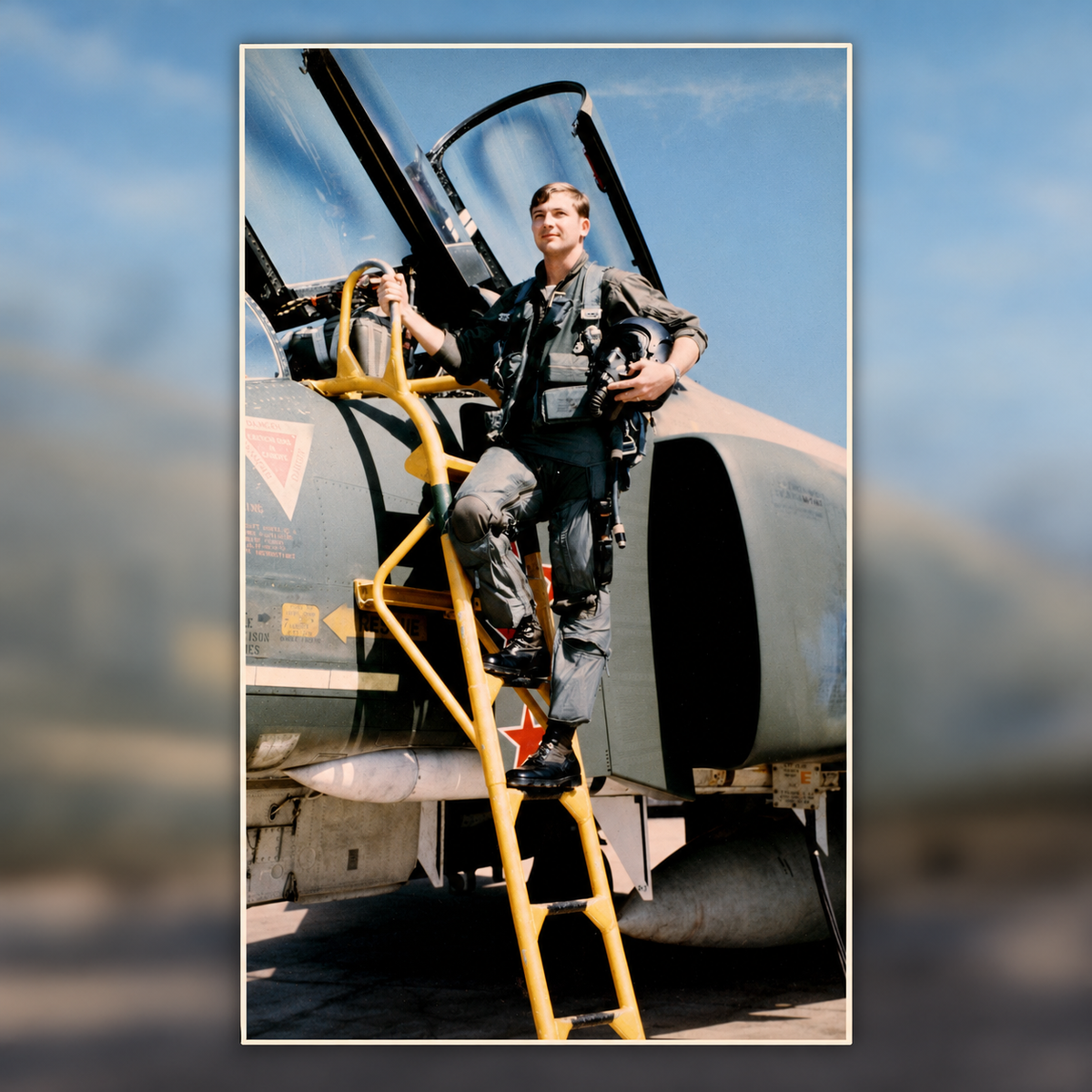 Captain DeBellevue in flight gear, holding his helmet while standing on a yellow boarding ladder beside the open cockpit of an F-4 Phantom II.